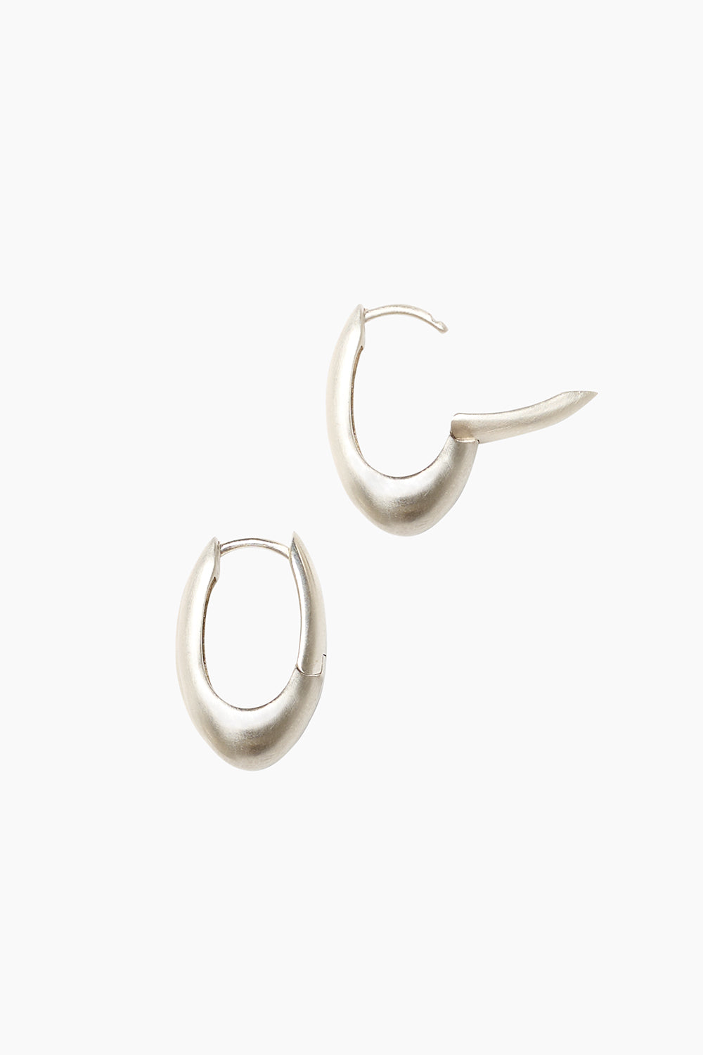 Sterling silver Keeper Earrings displayed at an angle, showcasing their elongated hoop design and fluid, organic curve with clasp detail visible.