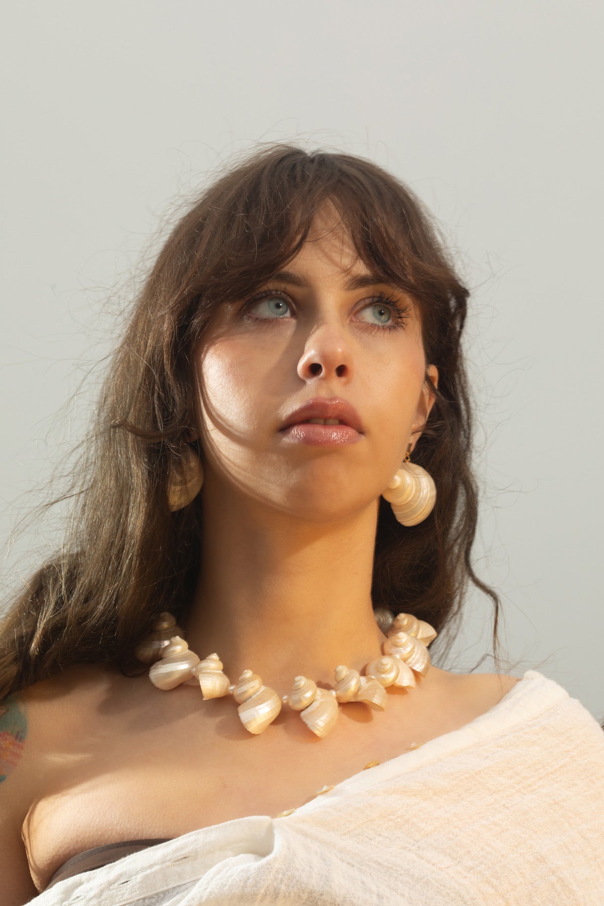 With her hair flowing in the wind, the model wears the Mer Necklace, a handmade statement piece featuring turbo seashells and freshwater baroque pearls. Paired with the Astr Earrings—gold-plated star studs with delicate turbo shell drops. Heirloom-quality pieces that will carry the essence of summer with you, from now until eternity.