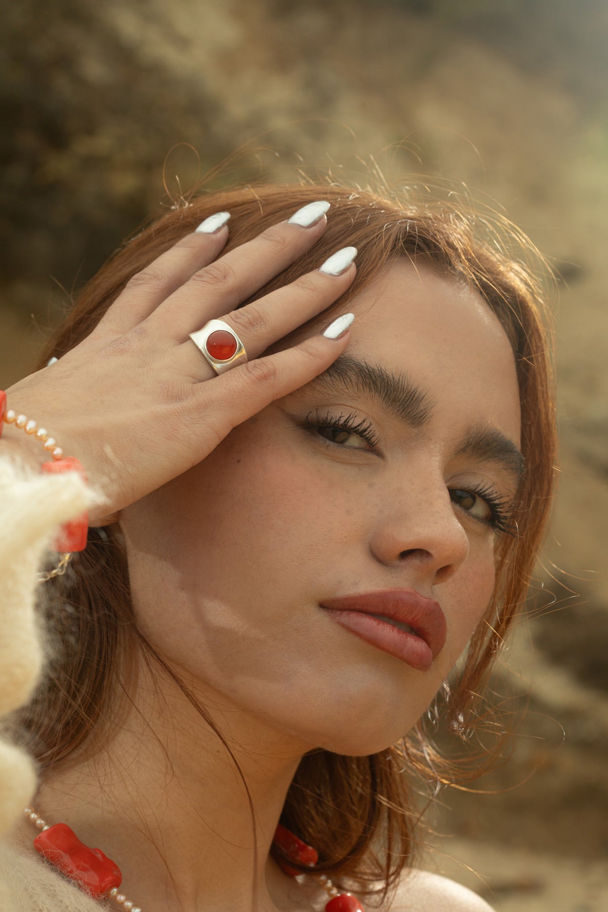Model wearing the Alexandra Ring in chunky sterling silver with a smooth carnelian cabochon, gently resting her hand against her face while looking at the camera.