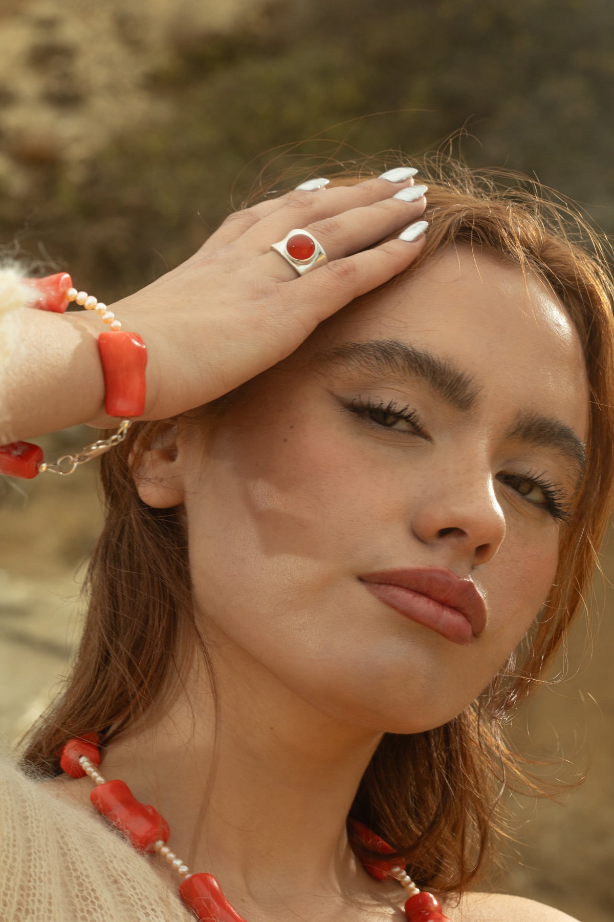 Model wearing the Alexandra Ring in chunky sterling silver with a smooth carnelian cabochon, gently resting her hand against her face while looking at the camera.