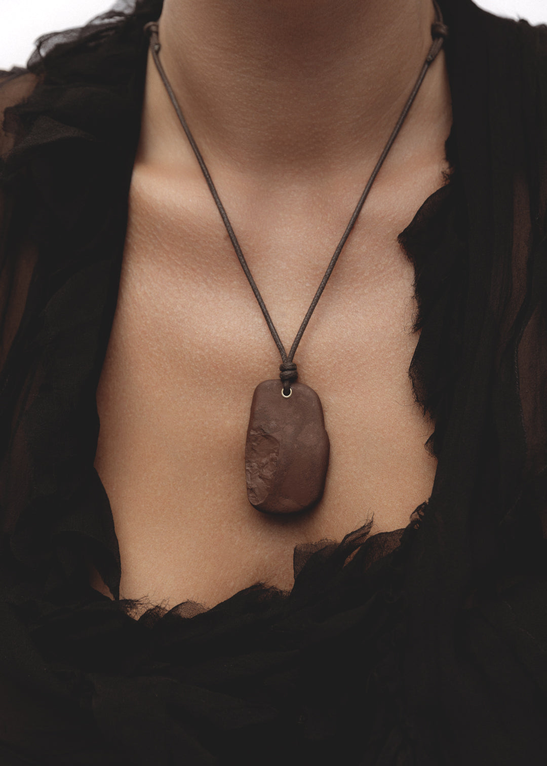 Model wearing the Erode Necklace — a burgundy stone pendant necklace on an adjustable dark brown waxed cotton cord with 14k gold-filled detail.