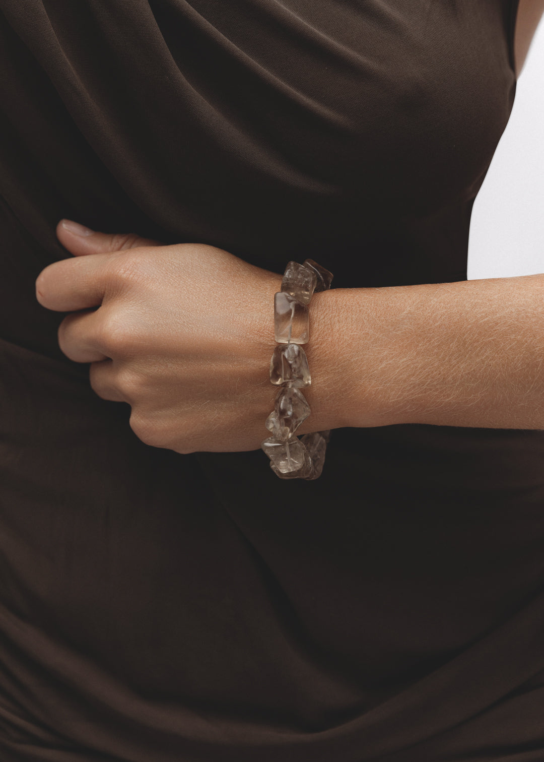 Fragments Bracelet in smoky quartz, with large tumbled smoky quartz gemstones in earthy grey-brown hues worn on the wrist, styled with a dark brown draped top.