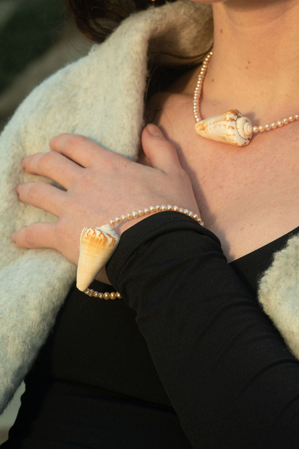 Close-up of a model posing with her arm draped across her chest, showcasing the Isla Necklace with freshwater baroque pearls and a conch shell pendant, paired with the matching Isla Mini Bracelet for a cohesive, ocean-inspired jewelry look.