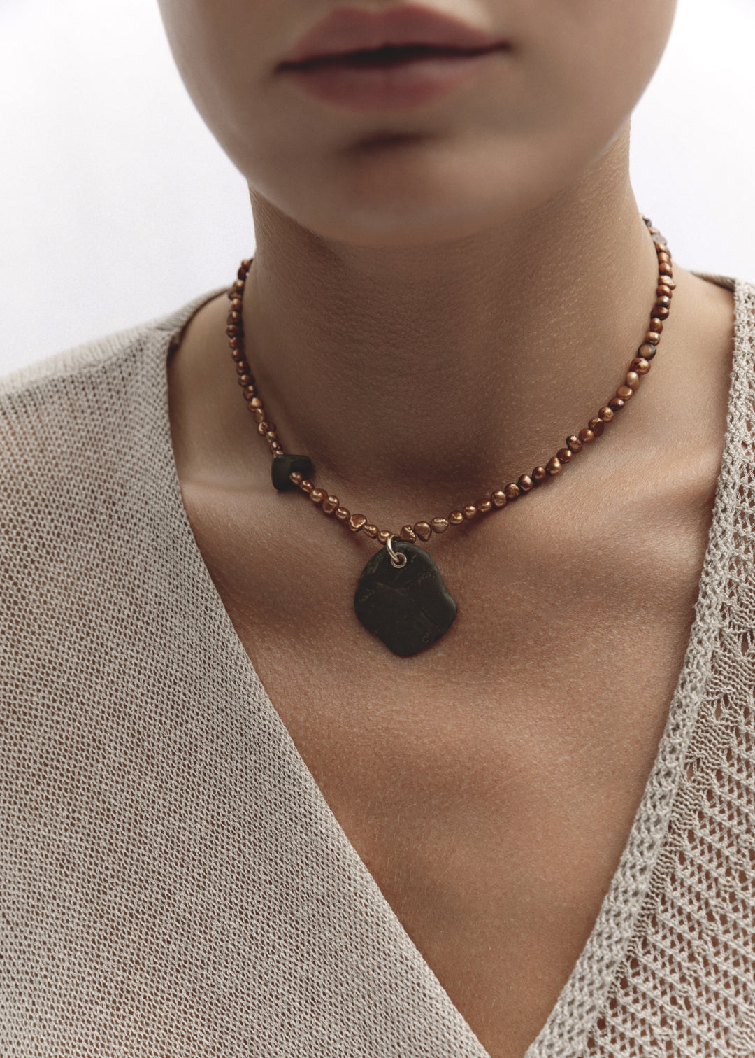 Model wearing the Ode Necklace — freshwater pearl necklace with a blue pebble pendant, styled against a neutral beige top.
