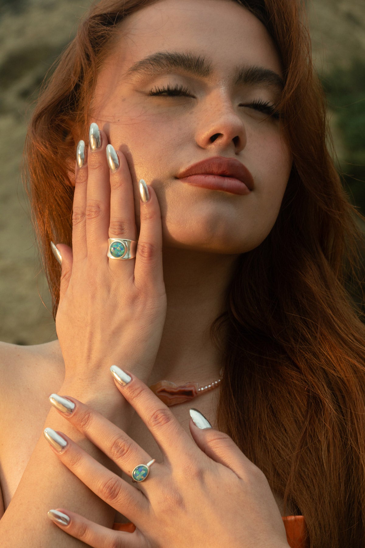The model's serene pose with eyes closed, showcasing both the Opal Mosaic II Ring and I Ring. Her hand rests gently on her face, paired with the Pia Necklace, a delicate freshwater pearl and Condor agate beaded piece. Together, they evoke the quiet beauty of ocean currents and sunlit shores.