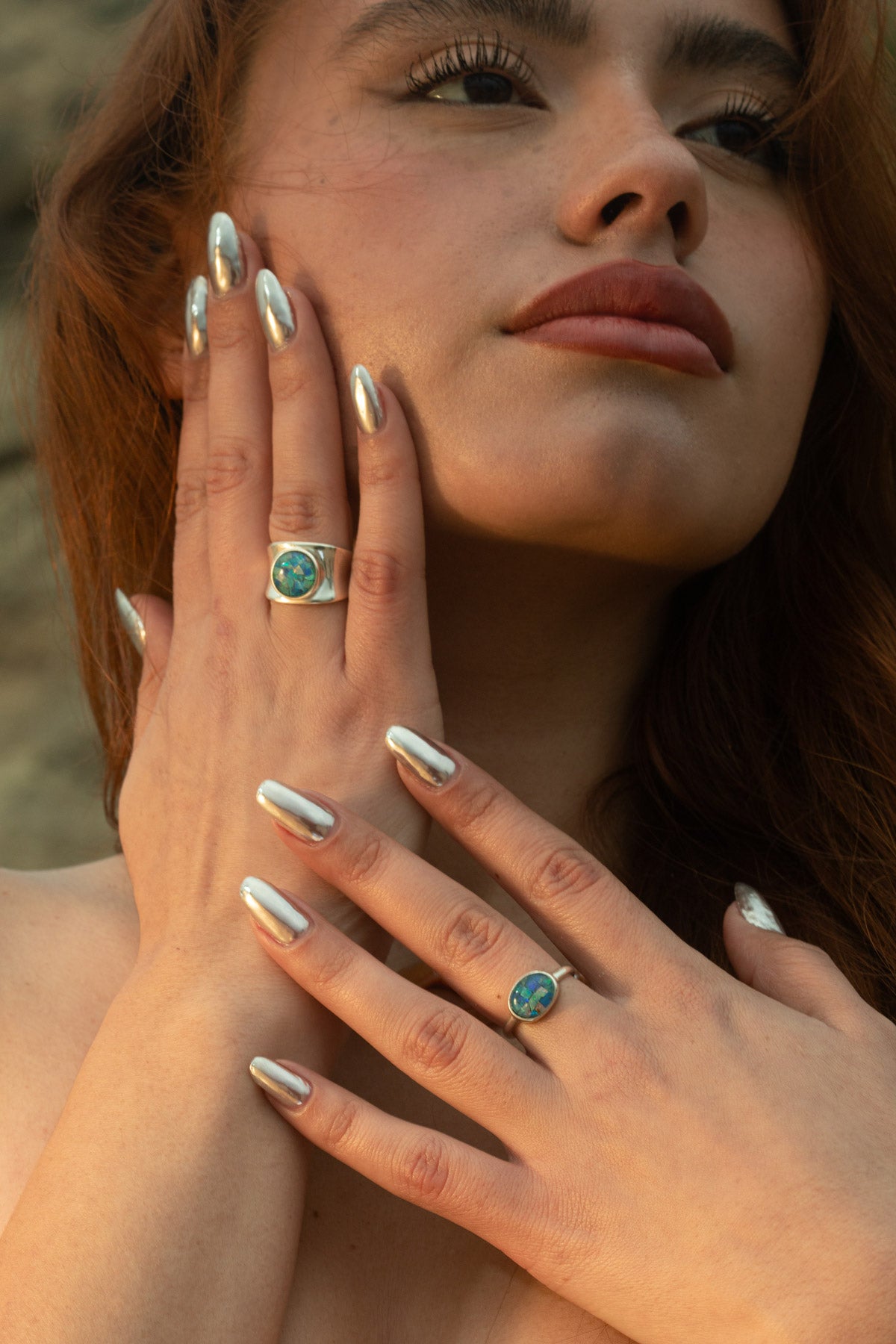 The model's serene pose with eyes closed, showcasing both the Opal Mosaic II Ring and I Ring. Her hand rests gently on her face, paired with the Pia Necklace, a delicate freshwater pearl and Condor agate beaded piece. Together, they evoke the quiet beauty of ocean currents and sunlit shores.