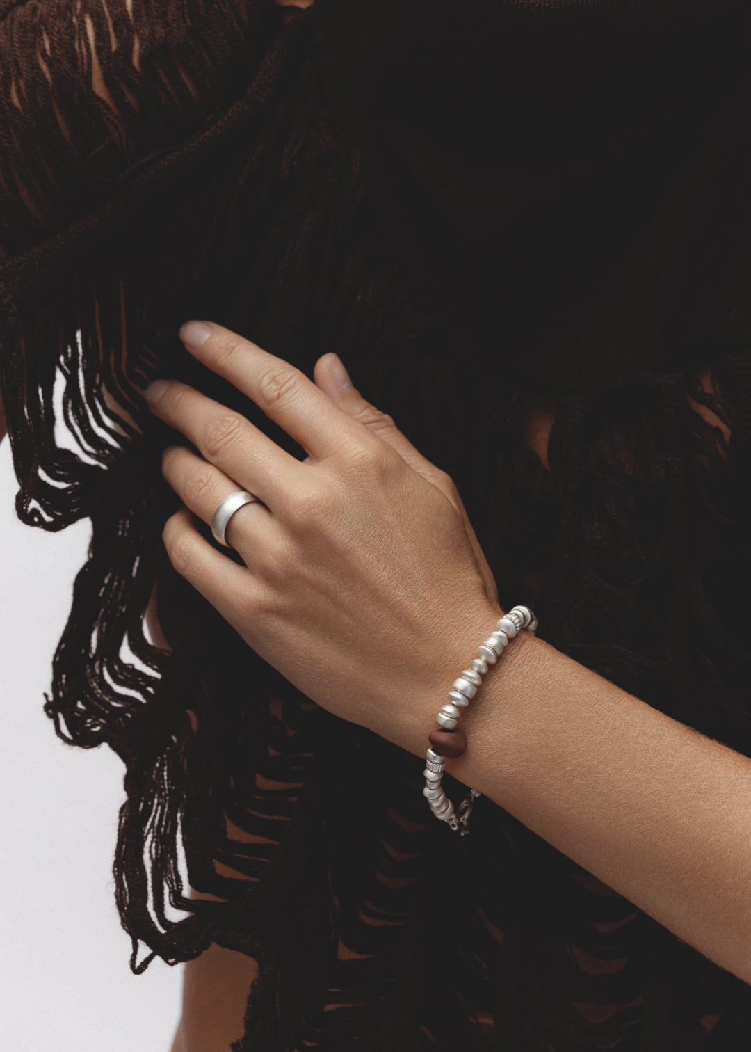 Model wearing the Pact Ring — a sterling silver cigar band ring with a wide, polished surface, styled on the hand against soft brown fabric.