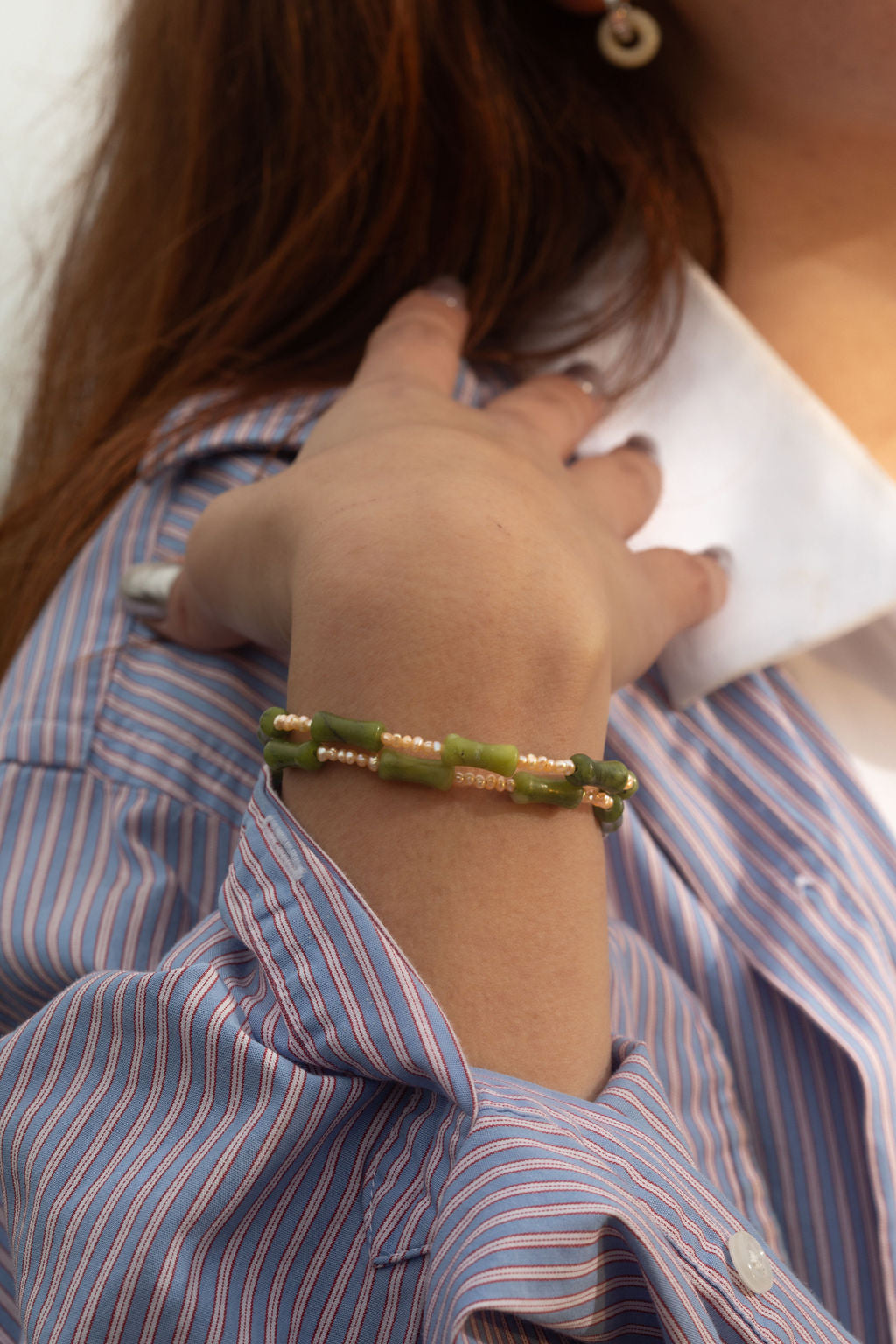 Close-up of model wearing the Santiago Bracelet, a handmade serpentine and freshwater pearl wrap bracelet. Her bent arm draws attention to its organic shapes and raw textures.