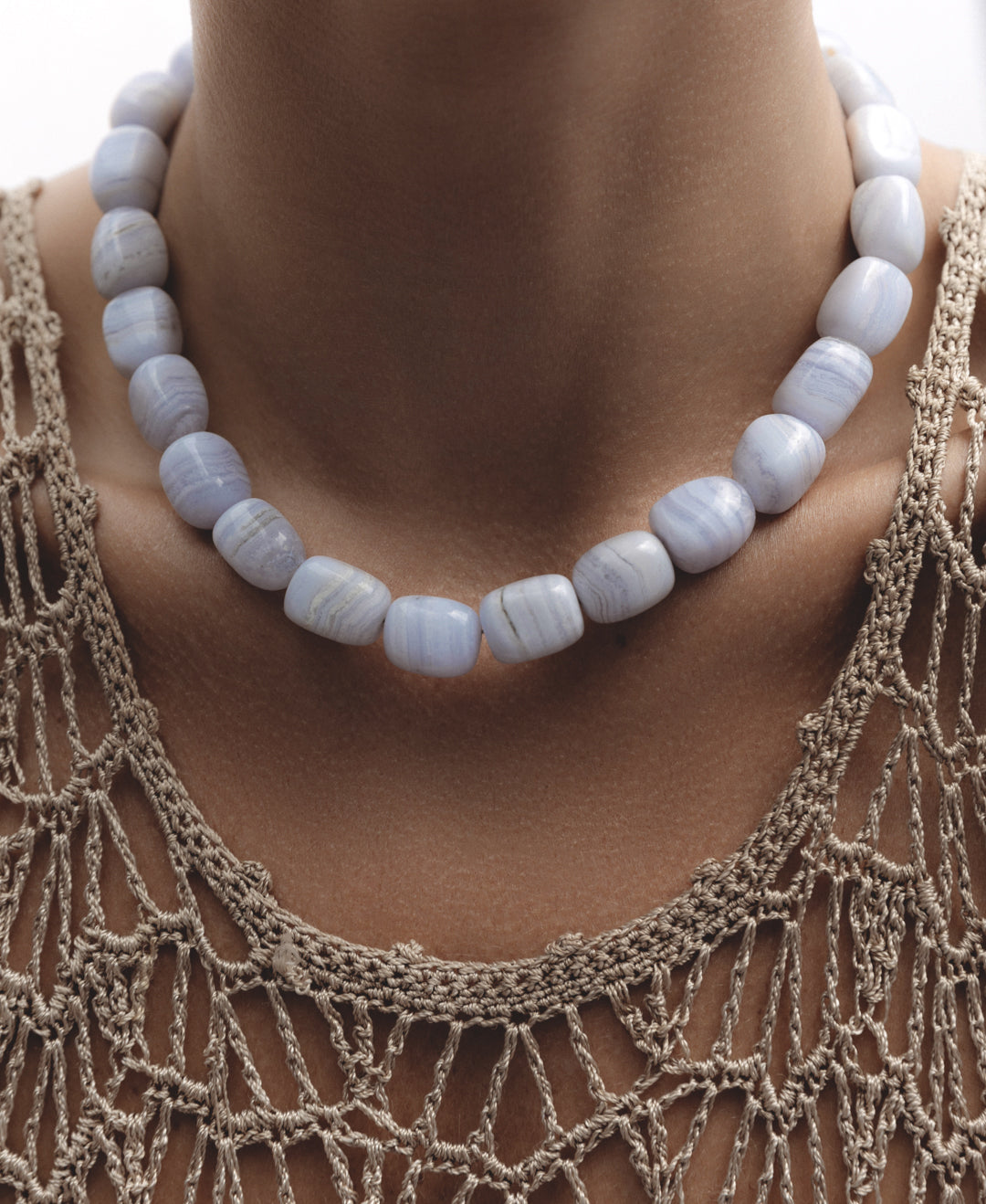 Model wearing the Vestal Necklace — bold chunky blue lace agate strand in soft blue and white hues, styled against a neutral beige top.