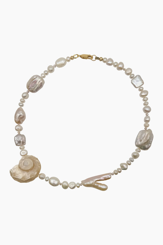 The Galiena necklace features freshwater pearls and an Angaria delphinus seashell, blending soft colors, organic shapes, and natural textures in a handmade design.