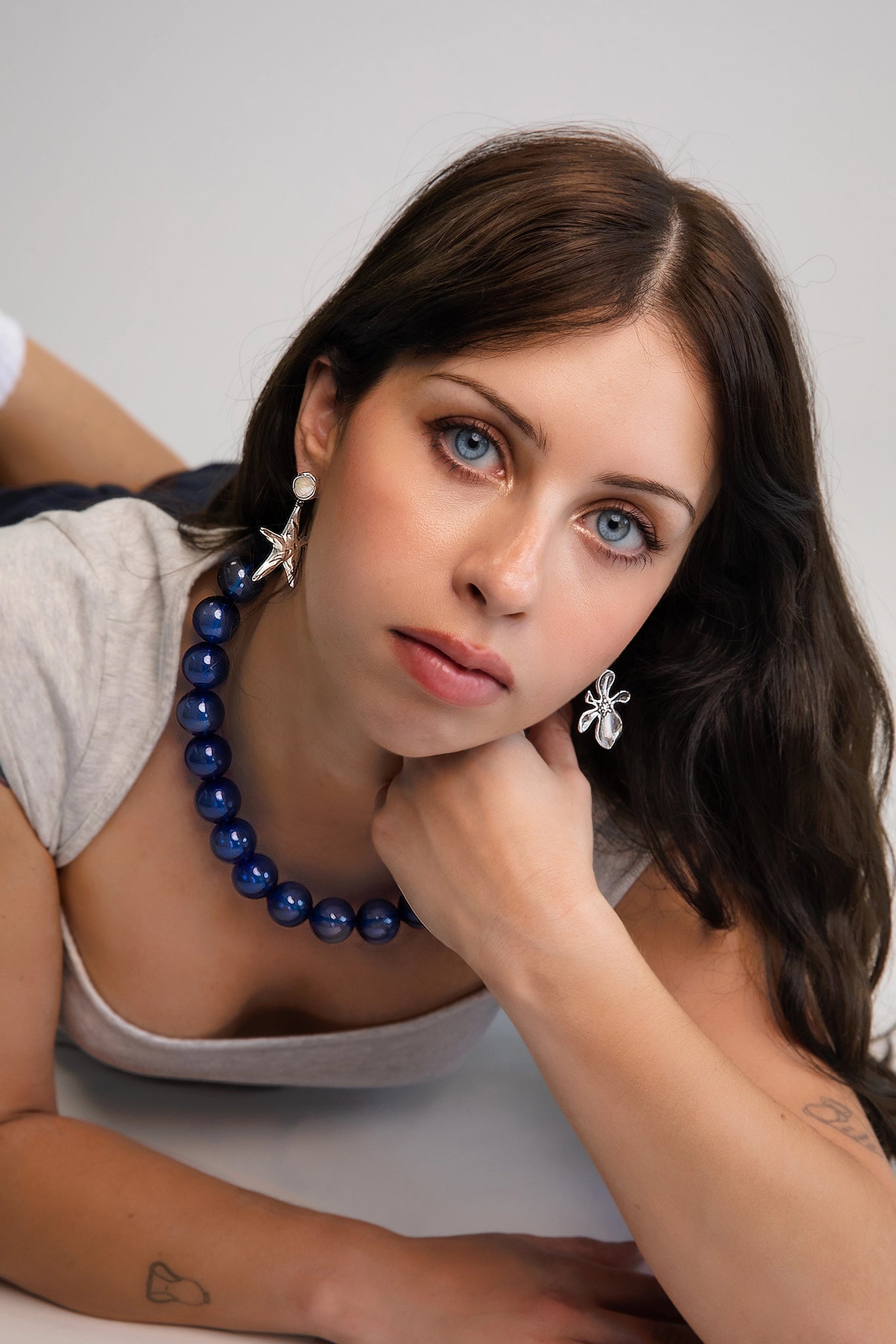 Model wearing mismatched hibiscus and starfish pendant earrings hand cast in Sterling Silver plating and suspended from freshwater pearls set in silver plating.