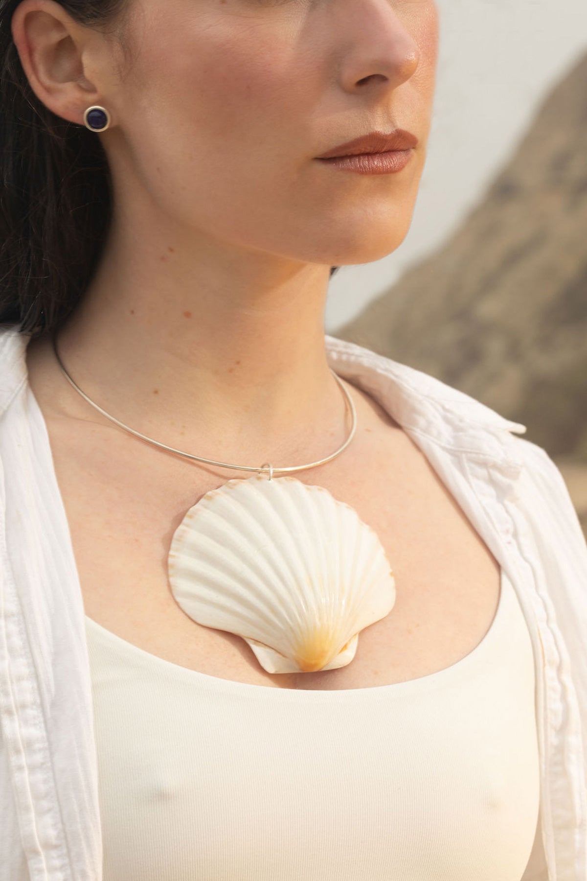 Model wearing the Mabel earrings, featuring blue lapis lazuli studs set in sterling silver. She pairs them with the Marina Necklace, a scallop shell pendant on a sterling silver neck wire. Timeless, heirloom-quality jewelry inspired by nature’s beauty.