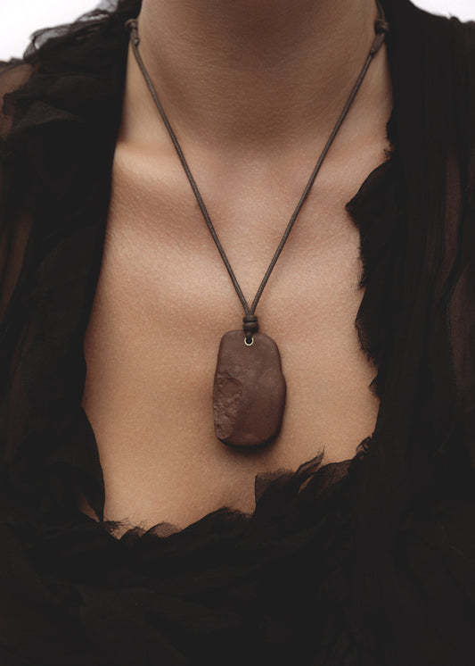 Model wearing the Erode Necklace — a burgundy  stone pendant necklace on an adjustable dark brown waxed cotton cord with 14k gold-filled detail.