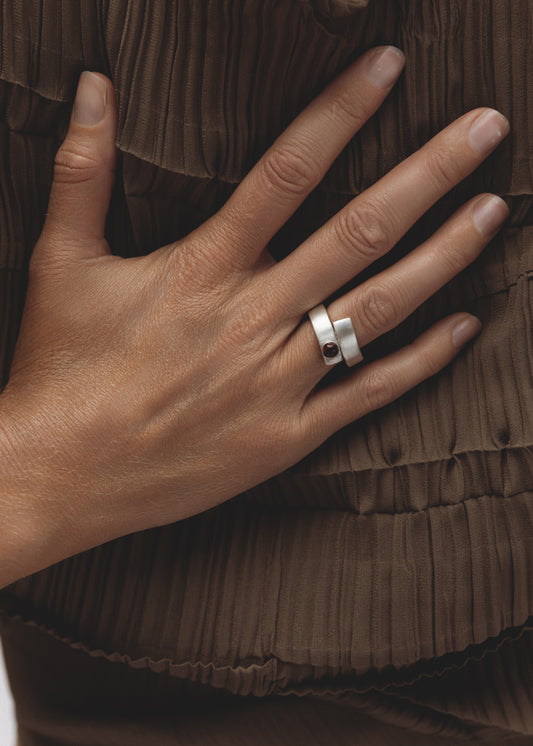 Model wearing the Fervor Ring — sterling silver bypass ring with garnet, styled as a bold sculptural statement on the hand.