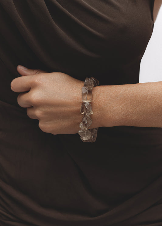 Fragments Bracelet in smoky quartz, with large tumbled smoky quartz gemstones in earthy grey-brown hues worn on the wrist, styled with a dark brown draped top.