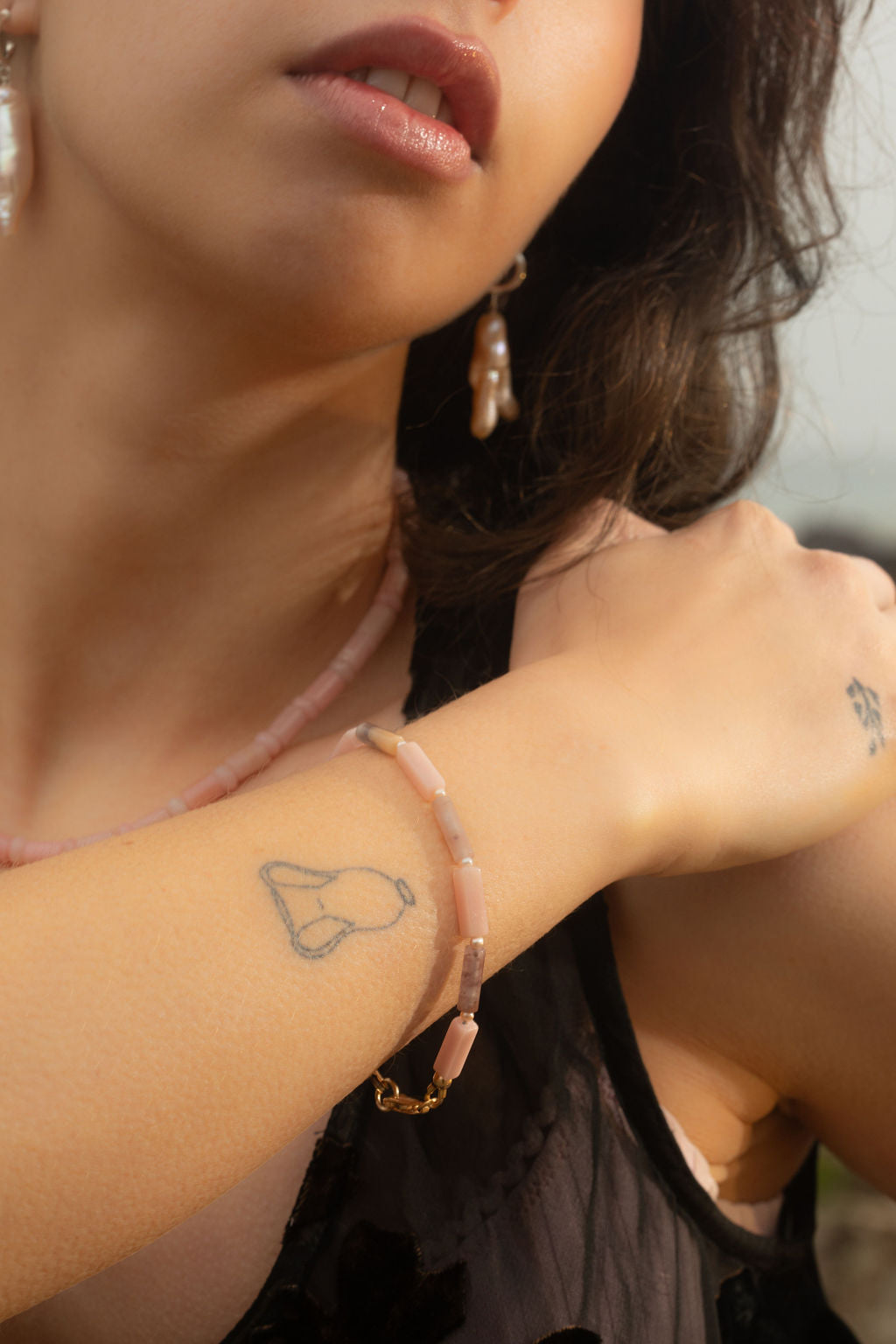 Close-up of the Gia Bracelet on a model’s arm draped across their shoulder, showcasing pink opal, phantom quartz, and freshwater pearls. The model looks away, emphasizing the bracelet’s organic textures and delicate design.