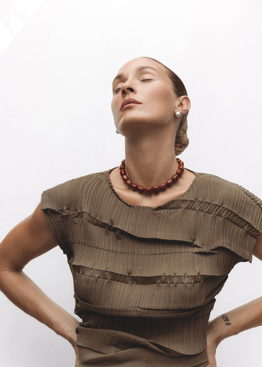Model wearing the Mantle Necklace — bold strand of tumbled red jasper gemstone beads in rich burgundy hues, styled against a neutral beige top.