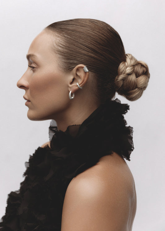 Model wearing the Memento Ear Cuff — a handcrafted silver cuff earring with a raw hammered texture, styled in an ear stack.