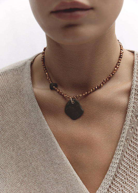 Model wearing the Ode Necklace — freshwater pearl necklace with a blue pebble pendant, styled against a neutral beige top.