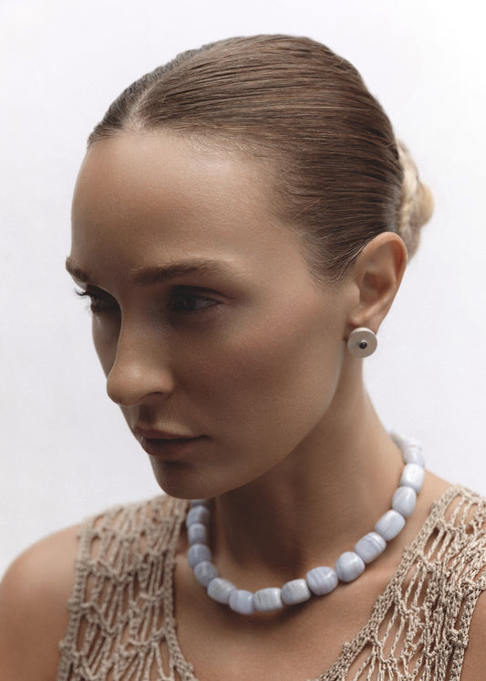 Model wearing the Oracle Earrings — sterling silver medallion studs with iolite, paired with a chunky blue lace agate necklace.