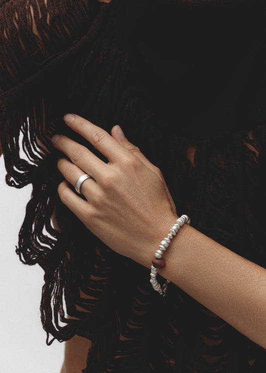 Model wearing the Pact Ring — a sterling silver cigar band ring with a wide, polished surface, styled on the hand against soft brown fabric.