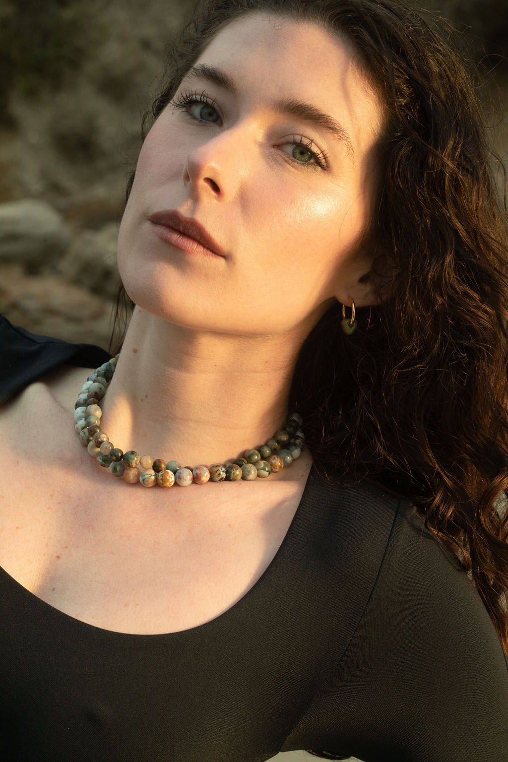 Close-up of model wearing the Pascal and Santal Necklaces. Ocean Jasper beads glow beside the moody eagle eye quartz, layered softly in golden hour light.