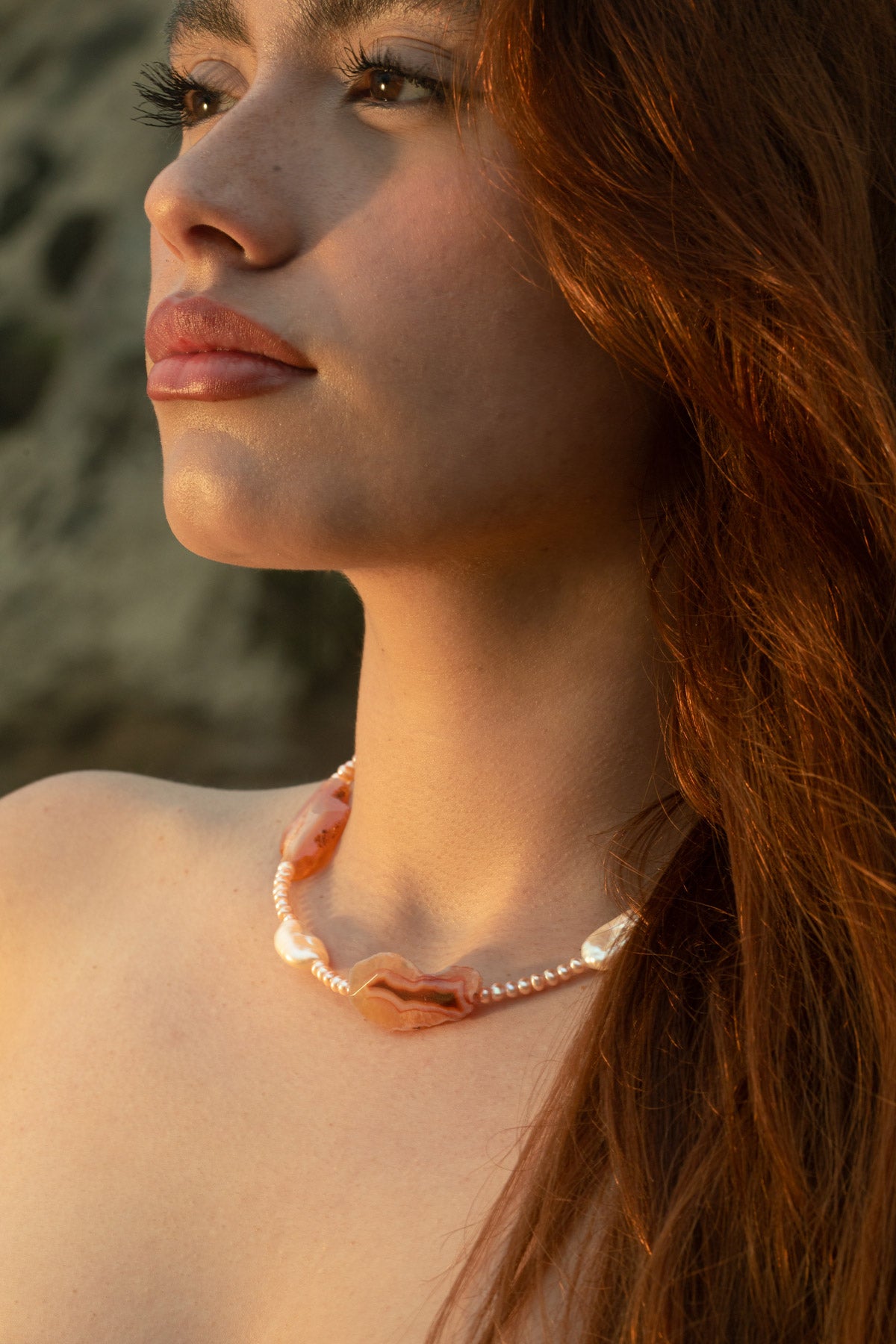In golden hour lighting, a close-up of the model highlights the Pia Necklace, crafted with Condor agate, freshwater keshi, and baroque pearls. Warm tones, artisanal, and quiet luxury.