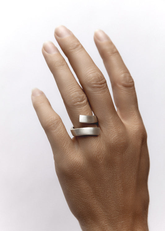 Model hand wearing the Vigil Ring, a bold sterling silver bypass ring with open negative space and matte finish for modern elegance.